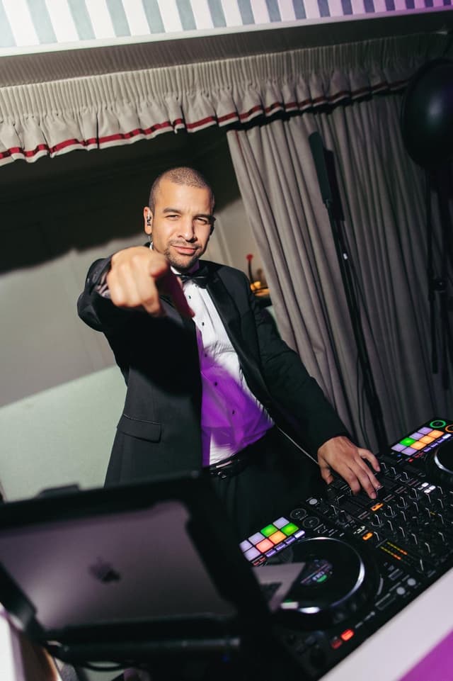 Austin Ventour in black tie behind the decks, pointing straight at the camera