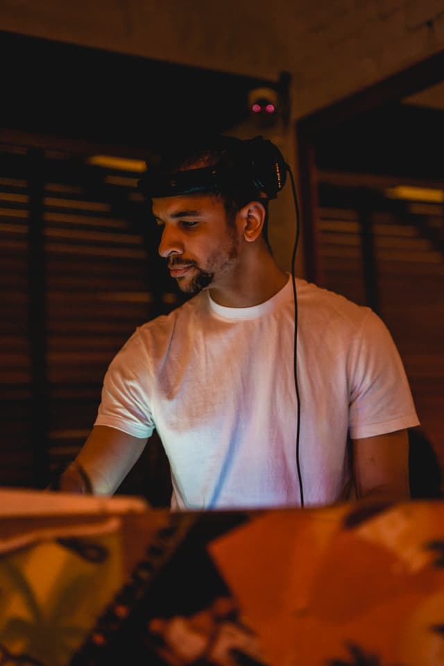 Austin Ventour in the DJ booth at night, headphones up, lit warm sodium orange