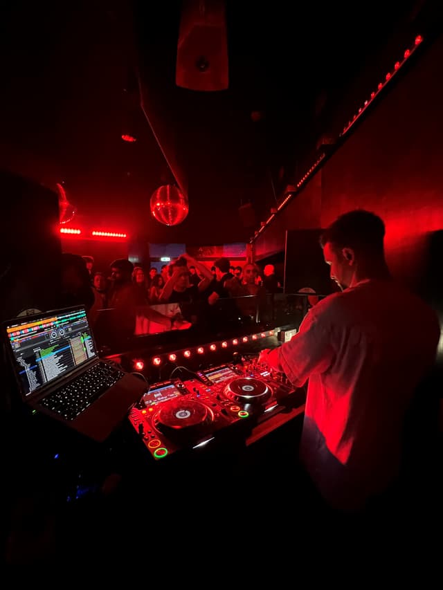 Austin Ventour at the decks in a red-lit club, a mirror ball over the dancefloor and the crowd up against the booth
